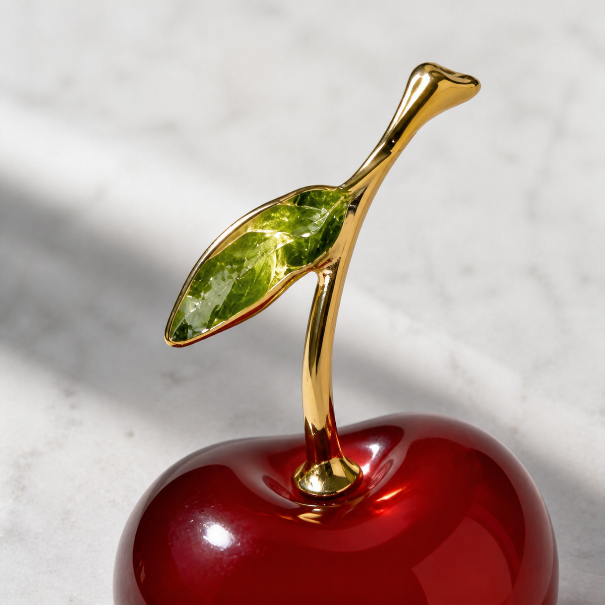 Close-up of the green glass leaf and gold-tone stem on the red cherry figurine